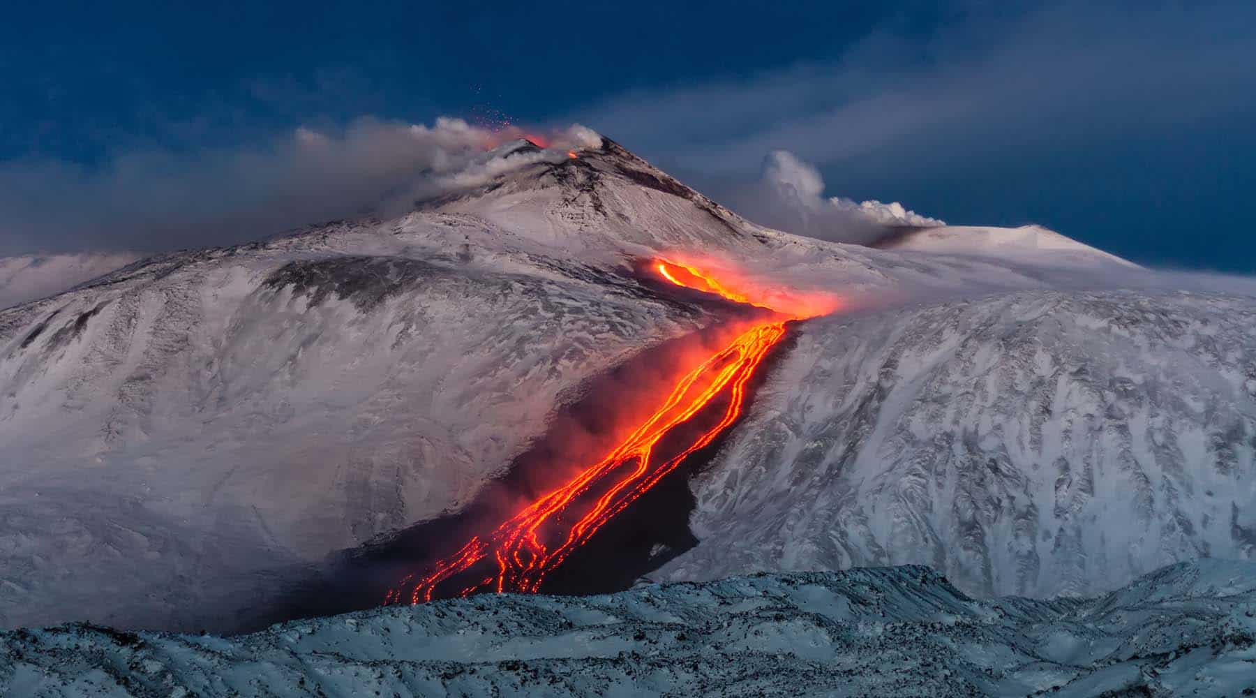 Picture of a volcano erupting and lava flowing down the mountain