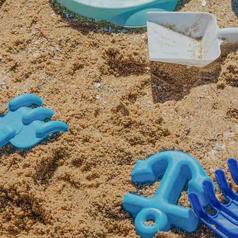 Children's sand toys including a white shovel, mold, and rake on sandy ground.